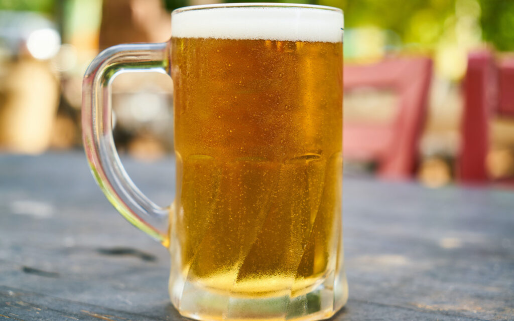 Pint glass of beer on a table, with chairs in the background.