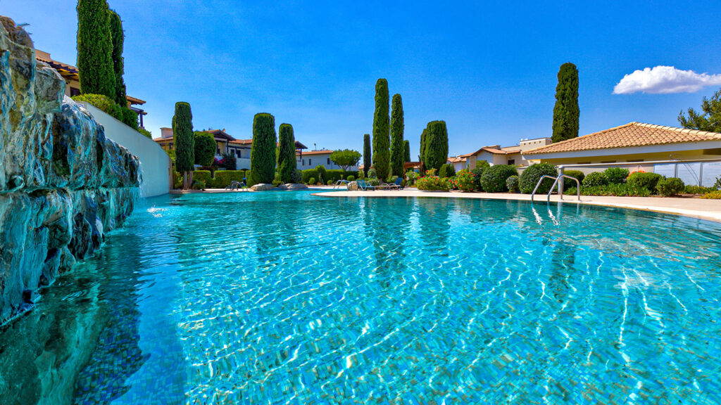 View of Helios Heights communal pool, water looking over to sun bathing terrace with lots of trees. Presented by Aphroditerentals.com.