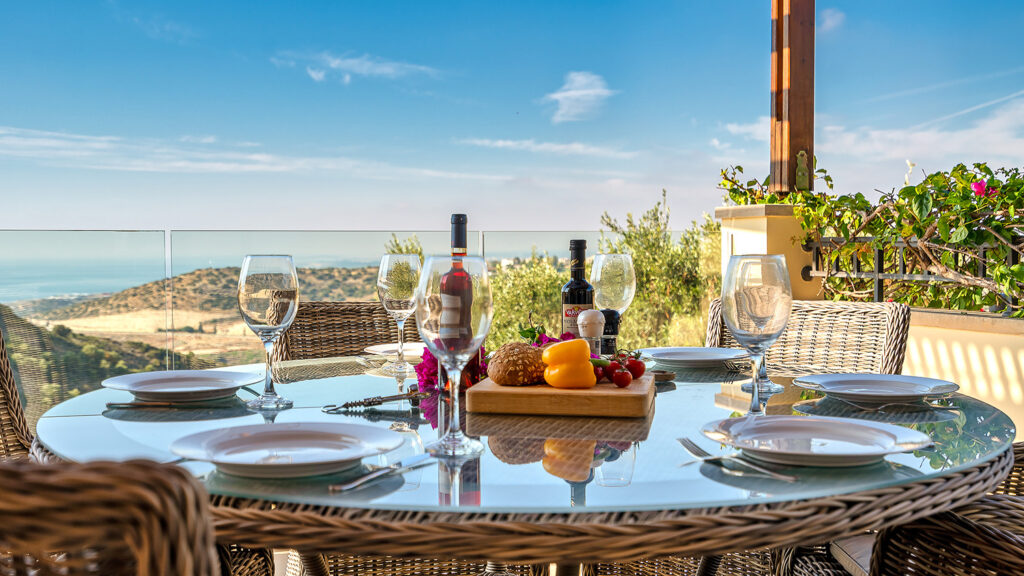 View of lunch table on balcony, with distant sea views and cloudy but bright sky. Presented by Aphroditerentals.com. Aphrodite Hills Resort, Cyprus.