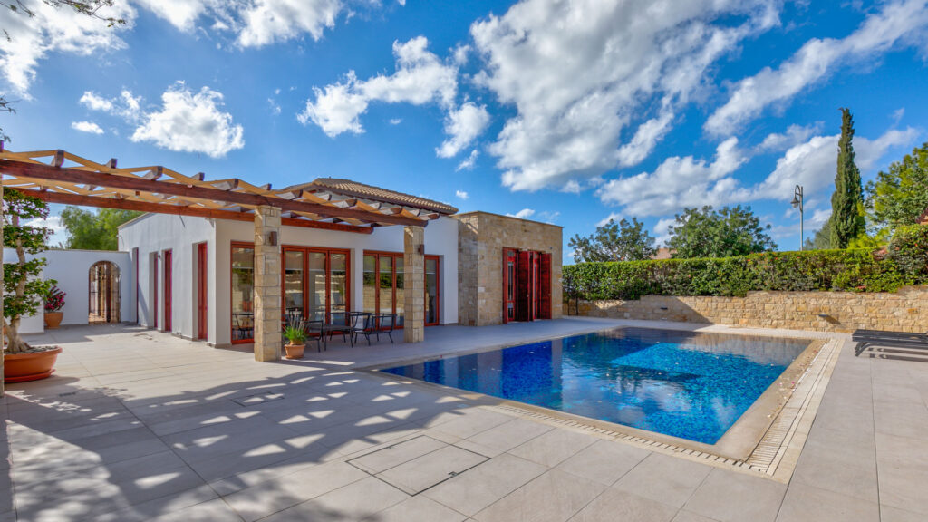 Front of villa building from corner of poolside terrace, showing overflow pool in foreground, and blue skies in background.