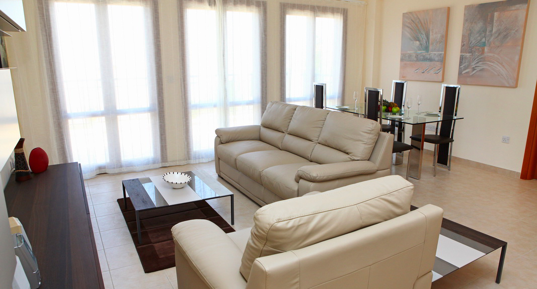 Photograph of living room of Apartment BG11 on Aphrodite Hills. Two cream leather sofas, tv and unit, coffee table and dining table and chairs.