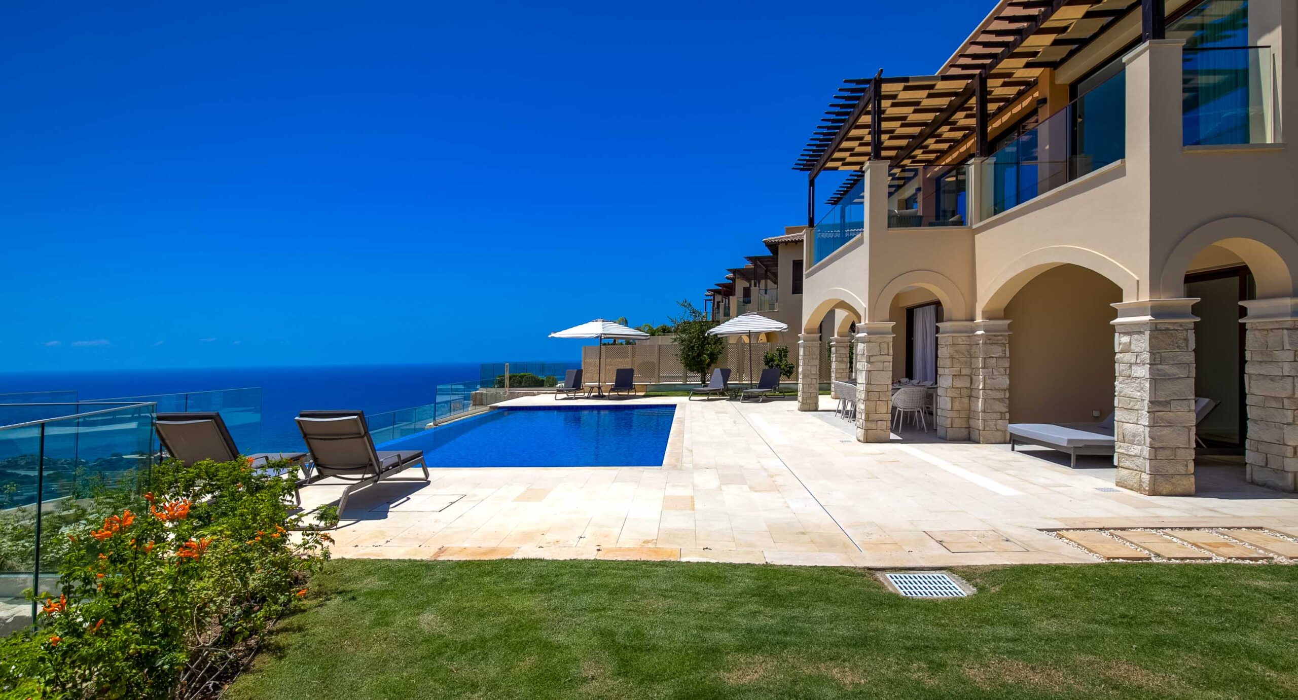 Villa Oniro UV09 - view of villa outside space from side; grass lawn, pool terrace and pool and villa building, with sea view in backdrop