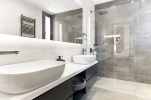 Photo of bathroom showing large mirror over double sink on left and modern walk in shower unit in the back