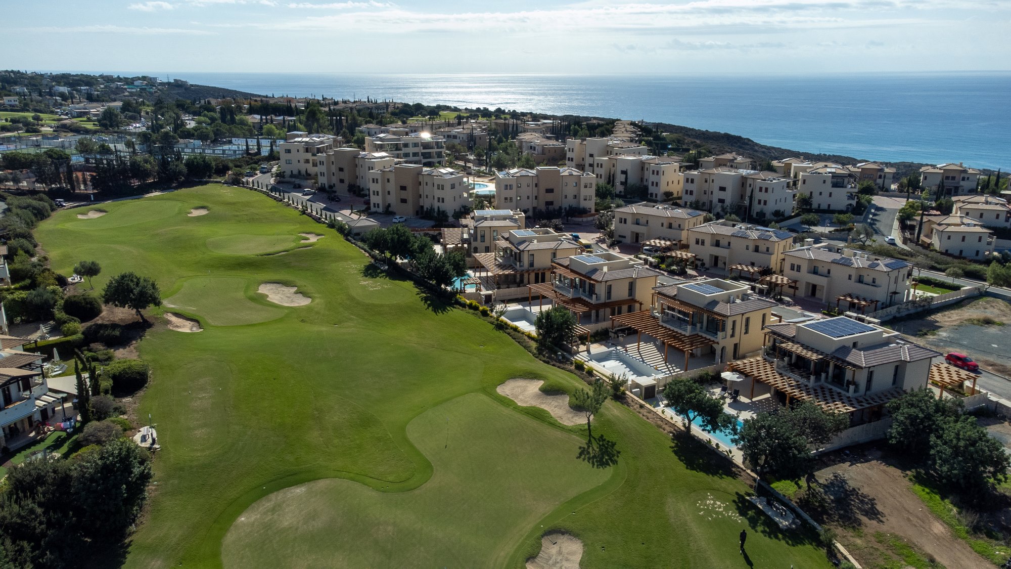 Aerial view of Dionysus Village on Aphrodite Hills - showing the golf course, surrounded by cream properties, and some swimming poosl, with the sea in the background.